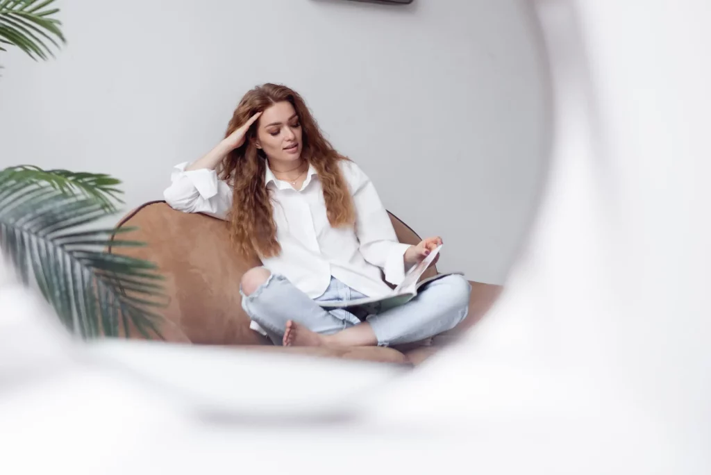 Mujer joven relajada leyendo en el sofá como parte del autocuidado promovido en las sesiones de fertilidad natural y psicología perinatal